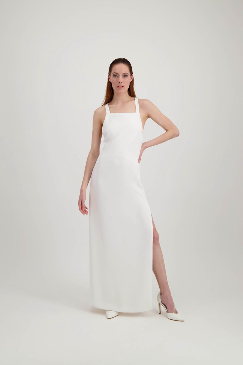 Jeune femme rousse, une main à la taille, habillée d'une longue robe blanche avec une fente et de larges bretelles