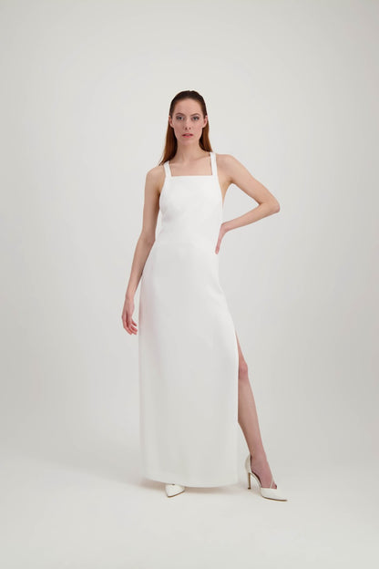 Jeune femme rousse, une main à la taille, habillée d'une longue robe blanche avec une fente et de larges bretelles