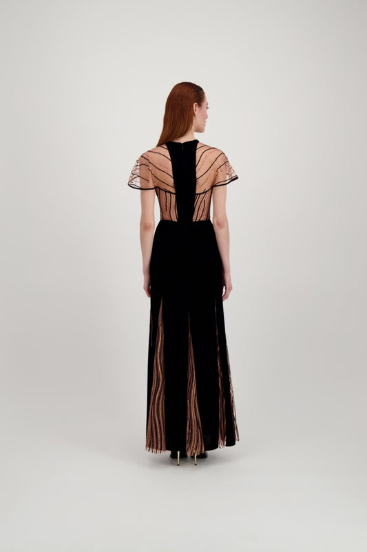 Jeune femme rousse de dos habillée d'une longue robe du soir en velours noir avec des motifs ondulés brillants.