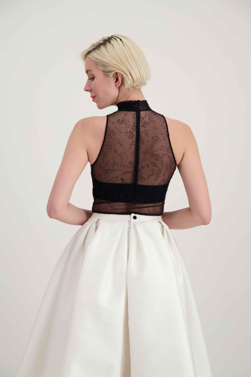 Jeune femme blonde de dos habillée d'un body transparent ras-du-cou et d'une jupe blanche