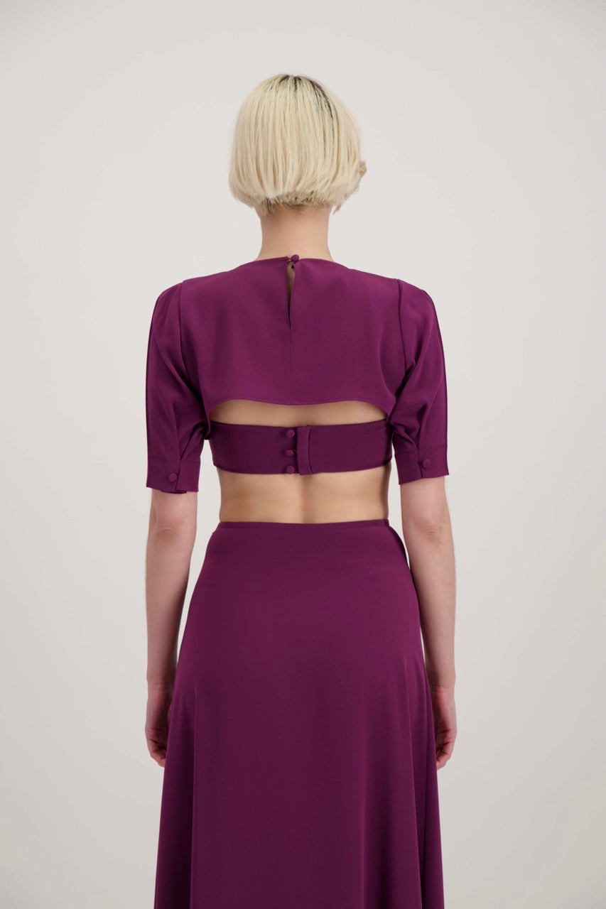 Femme blonde de dos habillée avec un ensemble composé d'un boléro, d'un bandeau et d'une jupe lila