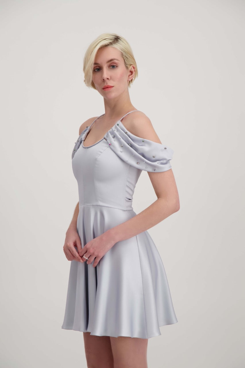 Jeune femme blonde de profil habillée d'une robe coktail courte de couleur argent avec des strass sur les épaules