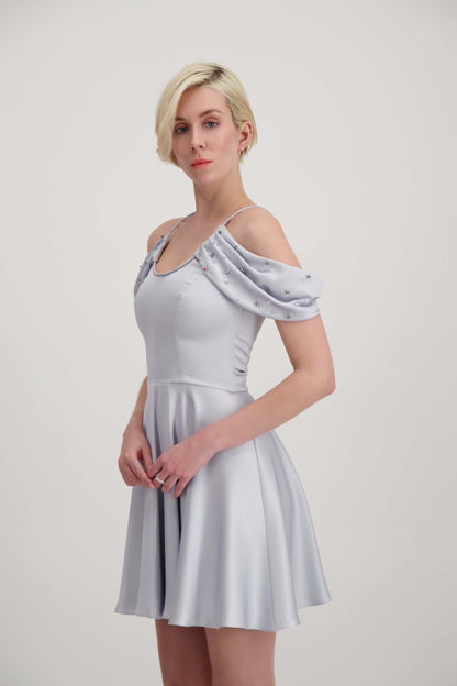 Jeune femme blonde de profil habillée d'une robe coktail courte de couleur argent avec des strass sur les épaules