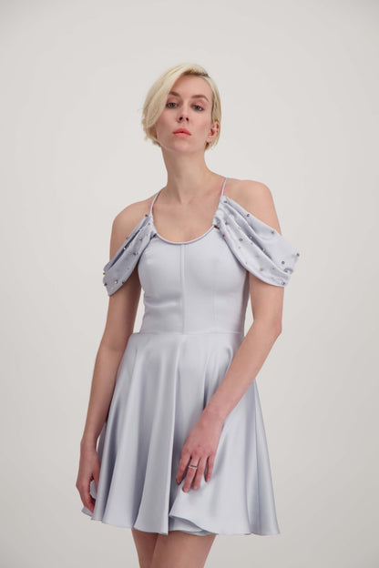 Jeune femme blonde habillée d'une robe coktail courte de couleur argent avec des strass sur les épaules