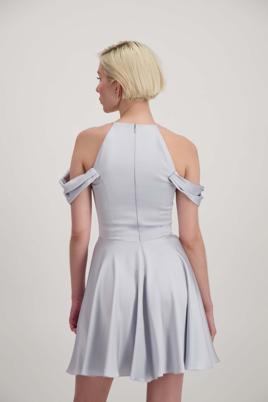 Jeune femme blonde de dos habillée d'une robe coktail courte de couleur argent avec des strass sur les épaules