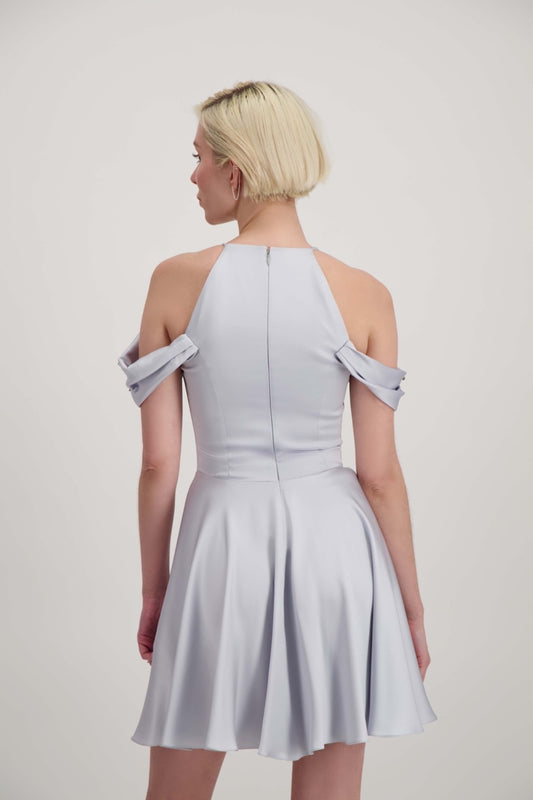 Jeune femme blonde de dos habillée d'une robe coktail courte de couleur argent avec des strass sur les épaules